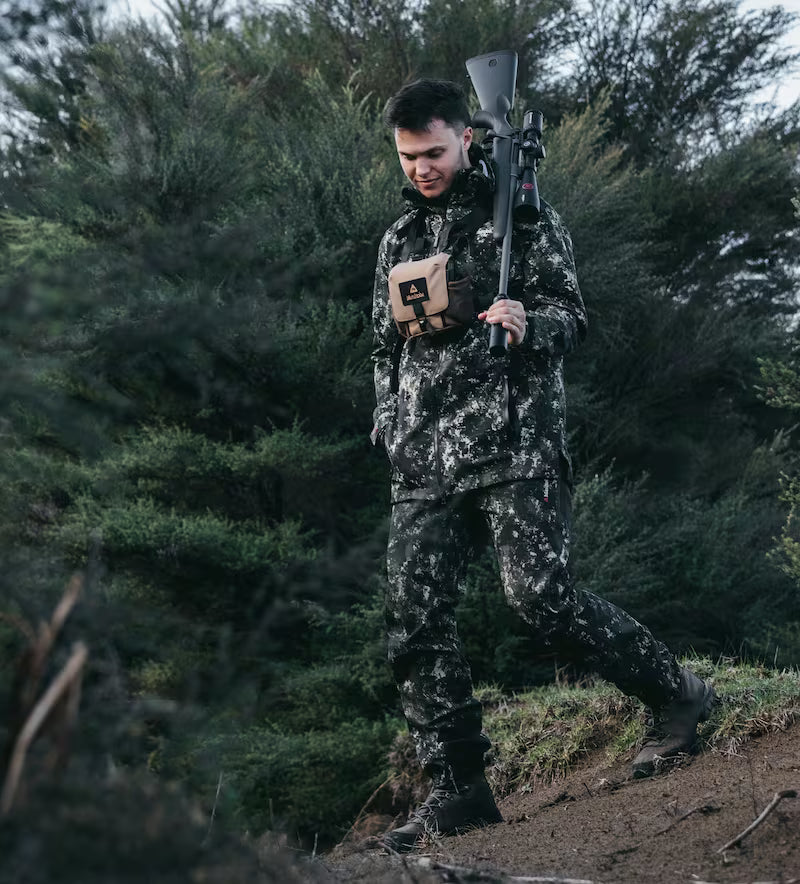 Man in camouflage walking through a forest with a rifle