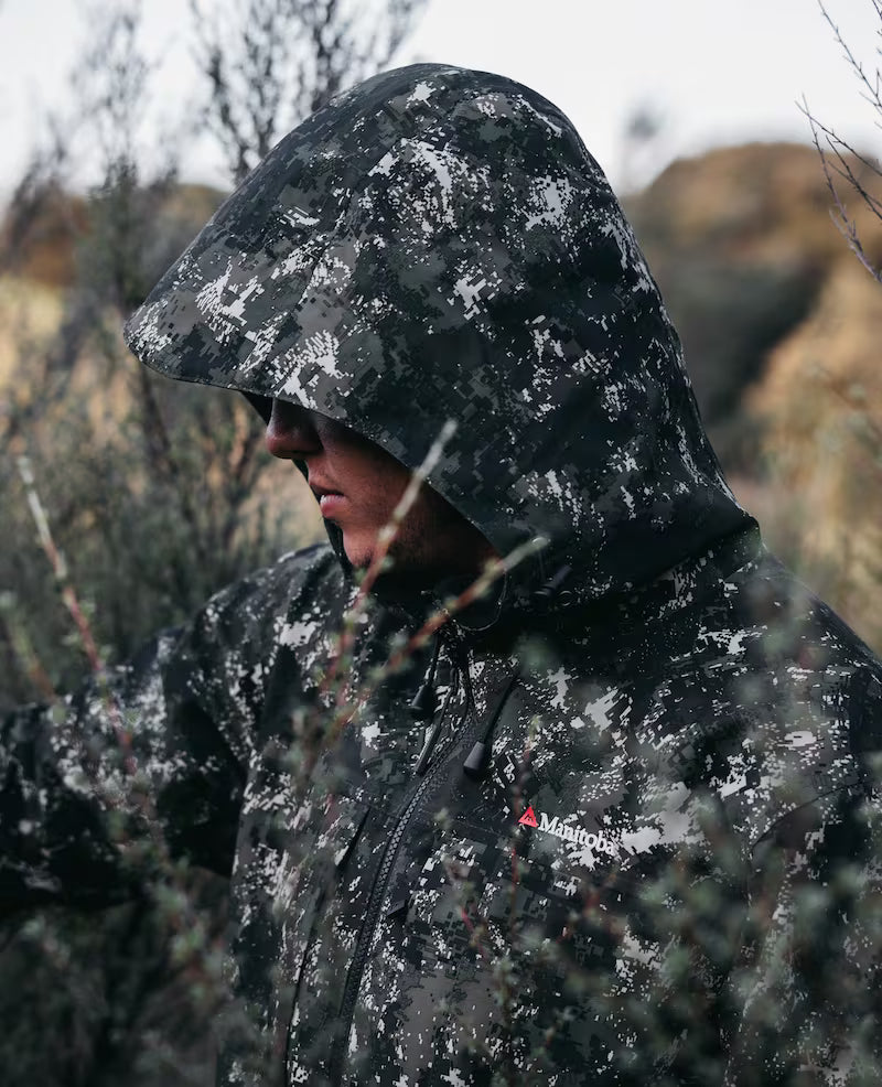 Person wearing a camouflage jacket with a logo in a natural setting