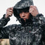 Person wearing a black and gray camouflage raincoat with a brand logo.