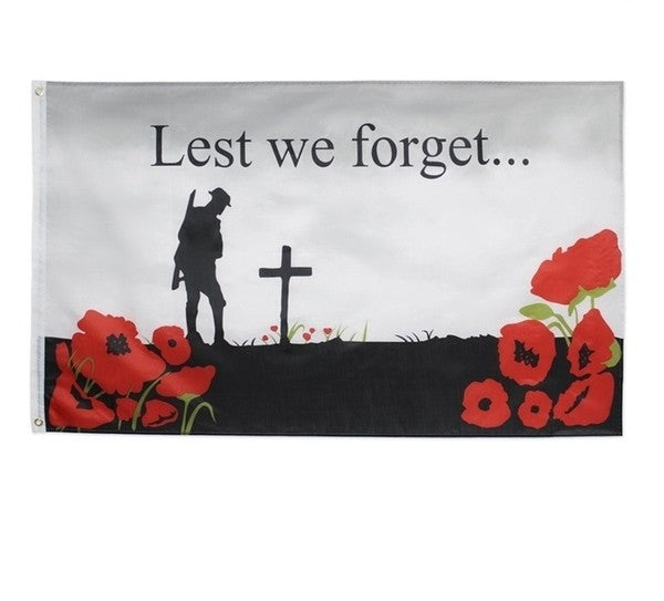 Memorial flag with silhouette of a soldier, cross, and red poppies with 'Lest we forget...' text.