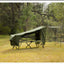 Green camping tent and table set up in a forested area with trees and grass.