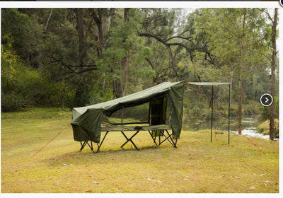 Green camping tent and table set up in a forested area with trees and grass.