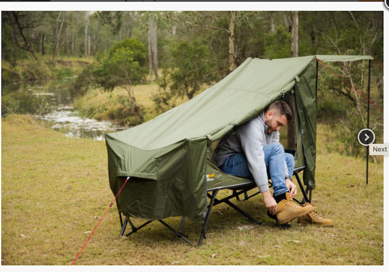 Man sitting on a green camping cot by a river with trees in the background