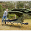 Man setting up a green camping cot in a forested area