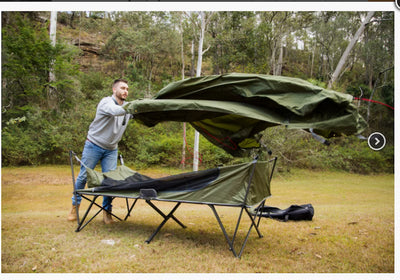Man setting up a green camping cot in a forested area