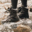 Person wearing brown boots walking through a shallow stream.