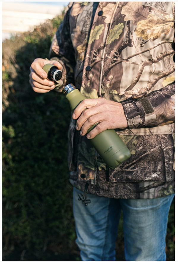 Person in camouflage holding a green water bottle outdoors