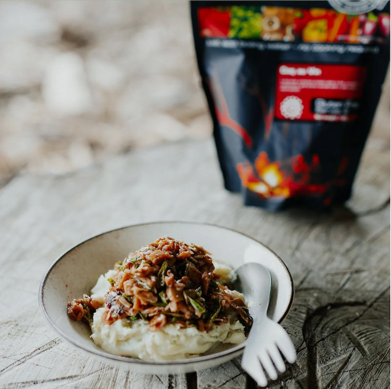 Bowl of food with a spoon on a wooden surface, with a package in the background.