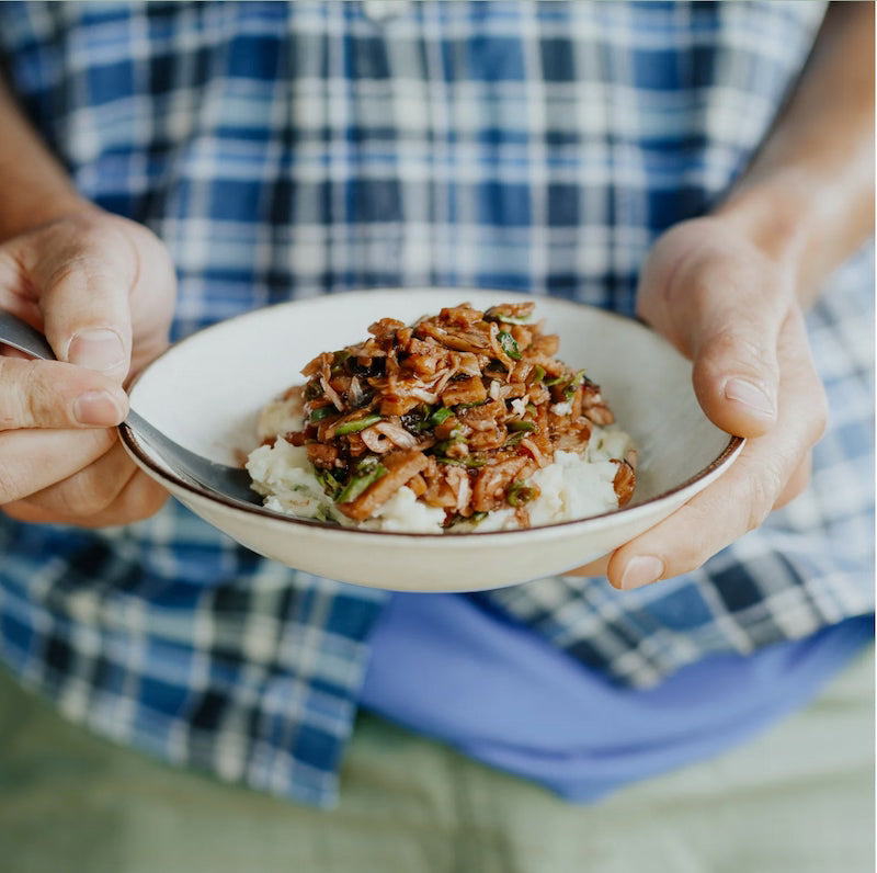 Person holding a bowl of food with a blue plaid shirt in the background