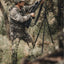 Hunter in camouflage gear with a rifle and tripod in a forest setting