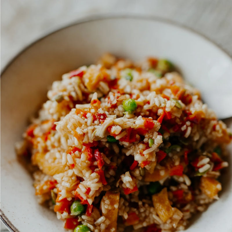 Close-up of a bowl of fried rice with vegetables on a white plate.