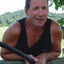 Man holding a black pole outdoors with greenery in the background