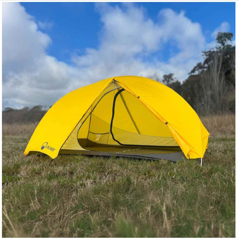 Yellow tent set up in a grassy field with a blue sky.