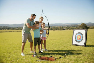 Family practicing archery in a field with a target in the background