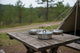 Camping scene with pots on a wooden table near a tent in a forest.