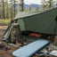 Camping setup with tent, backpack, sleeping pad, and cooking gear in a forest setting.