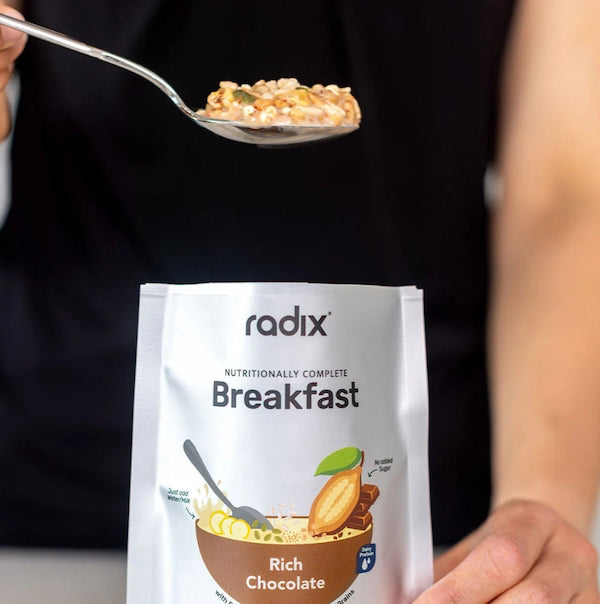 Person holding a spoonful of food above a radix breakfast package.