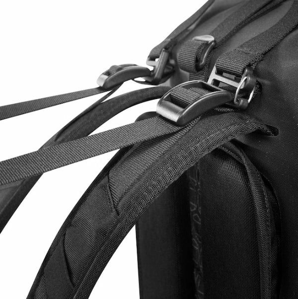 Close-up detail of a black backpack showing the webbing straps, plastic buckle closures, and textured fabric construction against a white background.