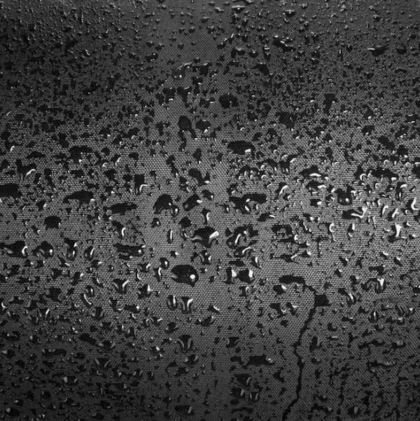 Close-up of a dark textured surface covered with scattered water droplets, shown in black and gray tones.