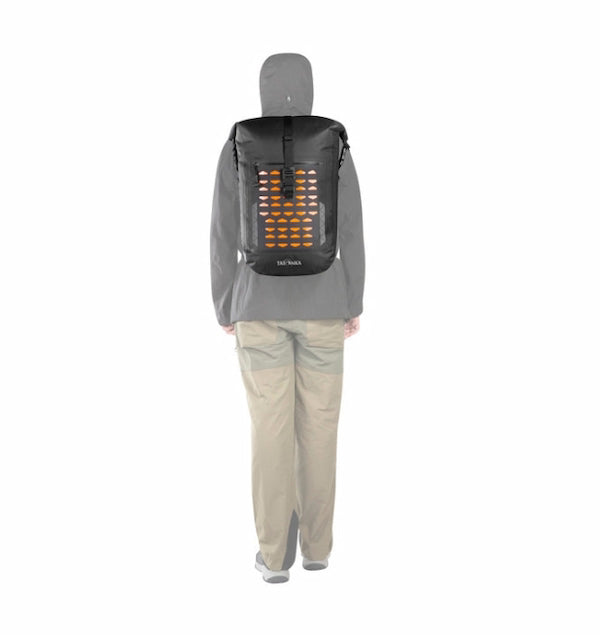 A person shown from the back wearing a gray hoodie and beige pants, carrying a black backpack with a glowing orange grid light panel on the back. The brand name 'Hot Shot' is visible near the bottom of the backpack.
