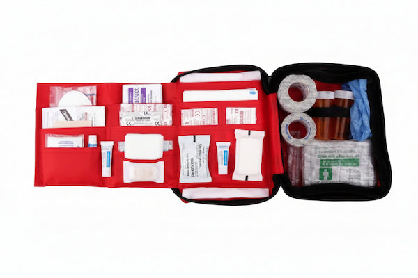 An open first aid kit with a red interior organizer and black outer casing, containing various medical supplies such as bandages, gauze, tape, and gloves, photographed on a white background.