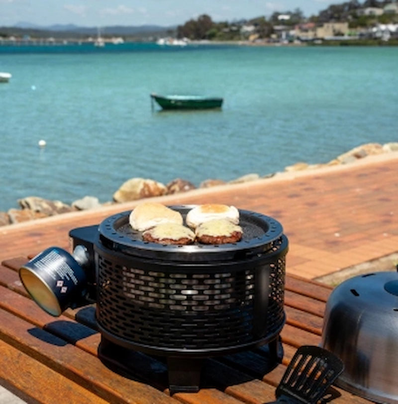 Portable grill with food on a wooden deck by a waterfront
