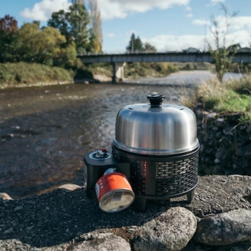 Portable stove with a pot on a stone ledge by a river with a bridge in the background