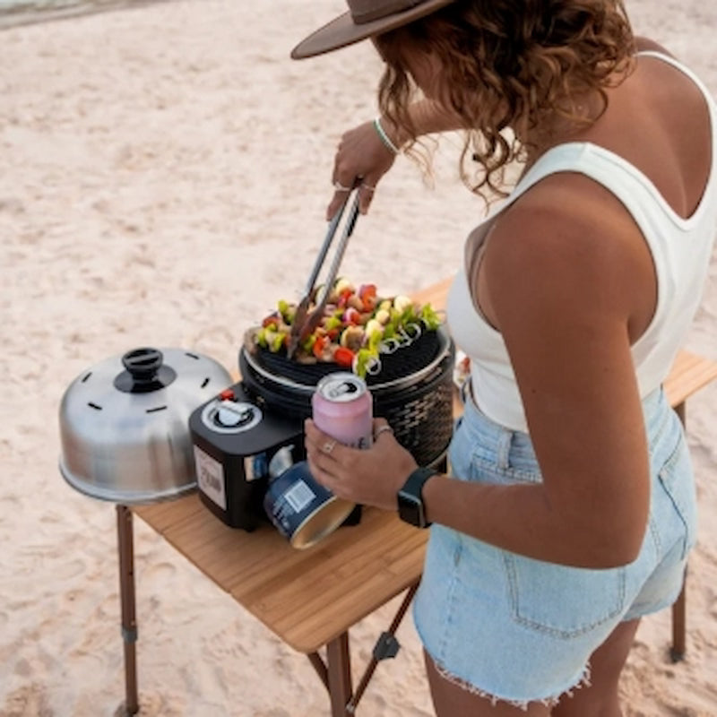 Person grilling outdoors with a pink drink can on a sandy background