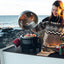 Person cooking pizza on a portable stove by the ocean
