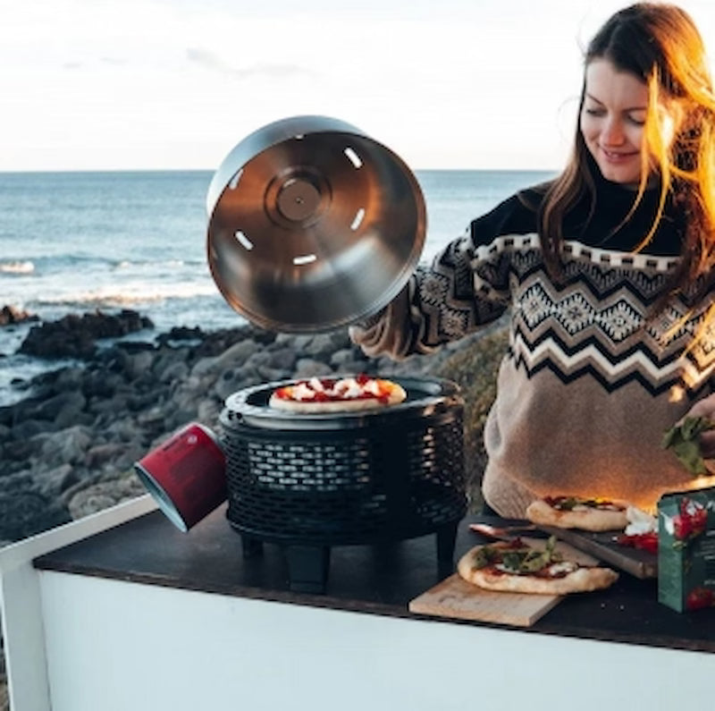 Person cooking pizza on a portable stove by the ocean