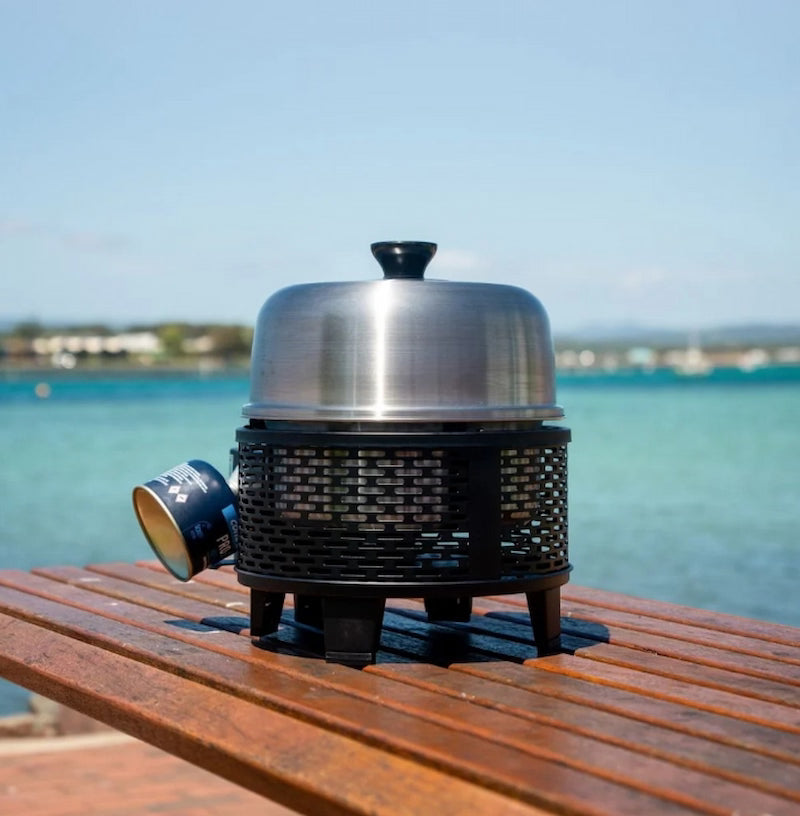 Portable grill on a wooden surface with a scenic background of water and sky.