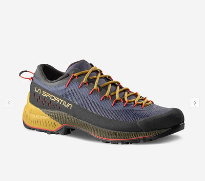 A single La Sportiva trail running shoe shown from a three-quarters angle against a light gray background. The shoe features a dark gray and navy blue mesh upper, mustard yellow laces, a yellow midsole, and red accents on the outsole and heel pull tab.