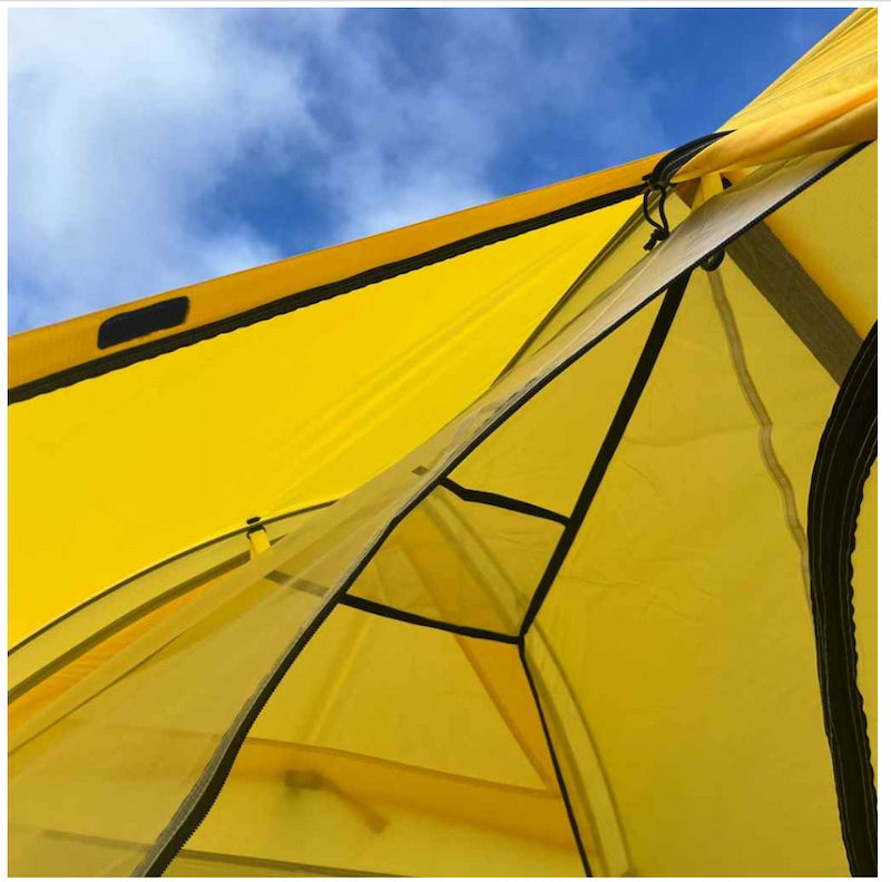 Yellow tent with a clear mesh door against a blue sky