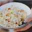 Close-up of a bowl with a white dish and red pepper pieces, held by a person.