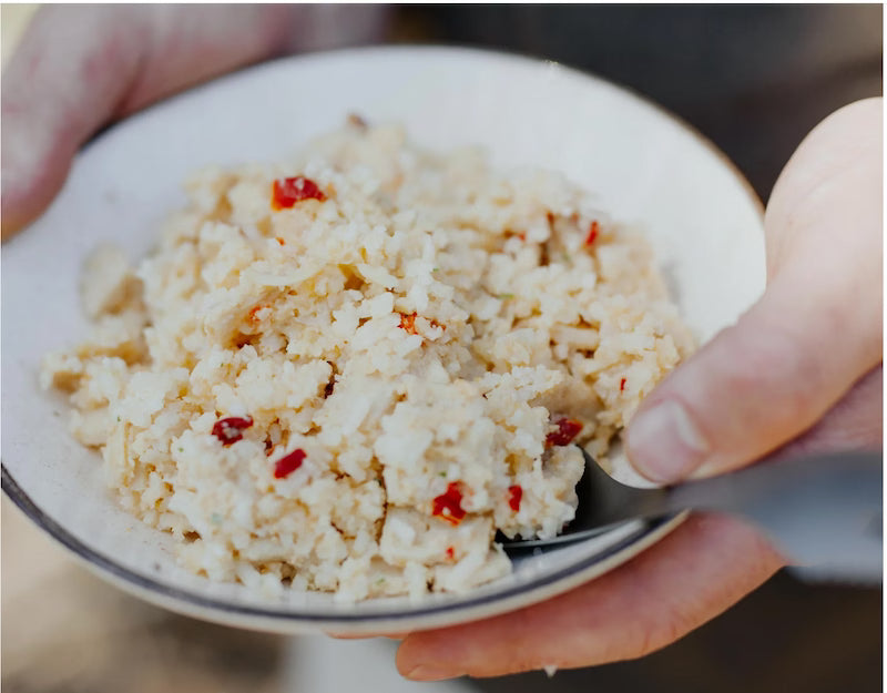 Close-up of a bowl with a white dish and red pepper pieces, held by a person.