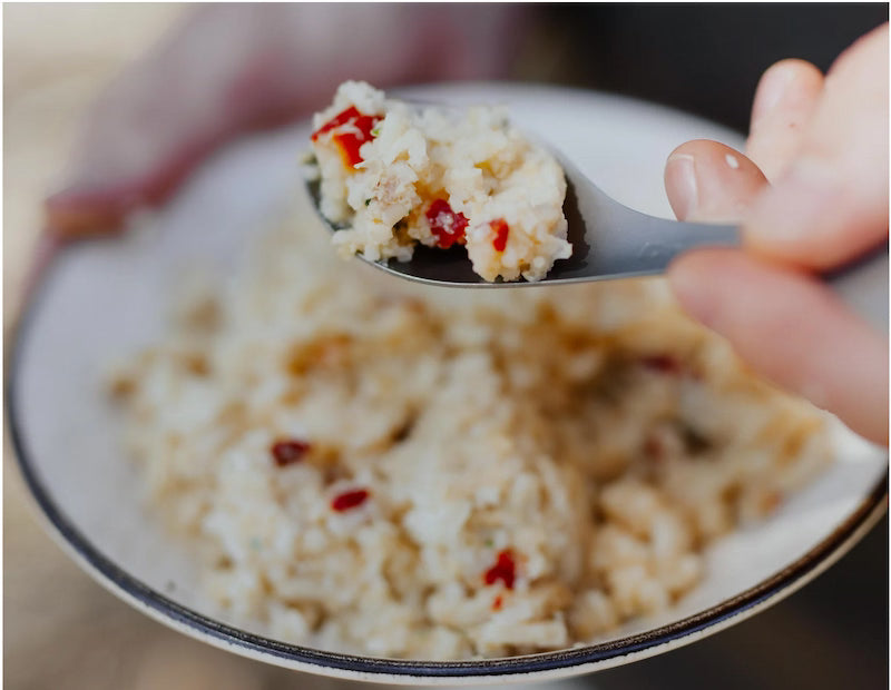 Close-up of a spoonful of rice with red peppers over a plate of rice.
