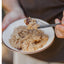 Person holding a bowl of oatmeal with raisins and a spoon