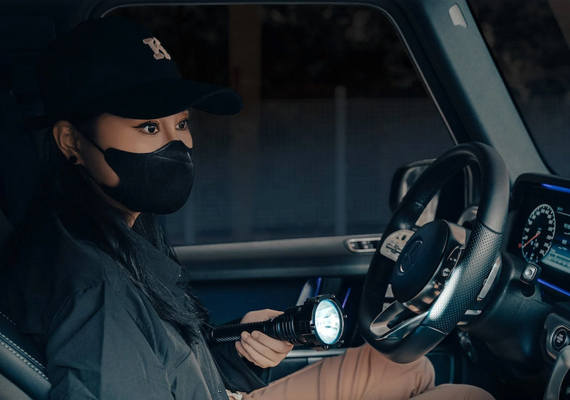 Person inside a vehicle holding a flashlight, wearing a black cap and mask.