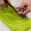 Person cutting green fabric with scissors on a white background