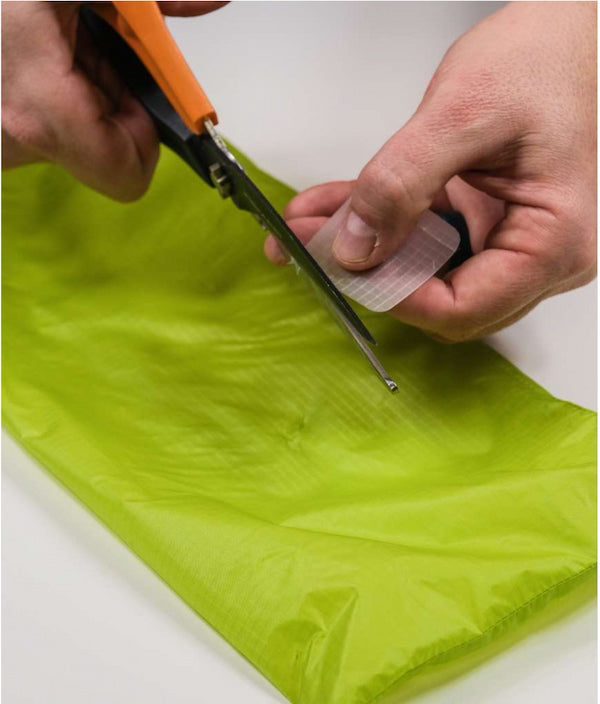 Person cutting green fabric with scissors on a white background