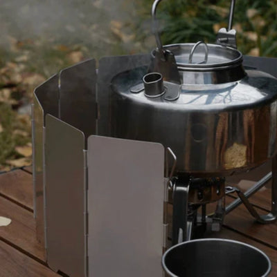 Stainless steel camping stove with a pot on a wooden surface outdoors