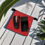 Red pouch with black stapler and phone on a light wooden surface with green leaves.