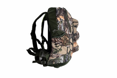 A camouflage backpack shown from the side against a plain white background, featuring a woodland tree-bark pattern in beige, brown, green, and black with dark green straps.