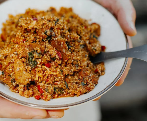 Person holding a bowl of quinoa salad with a spoon