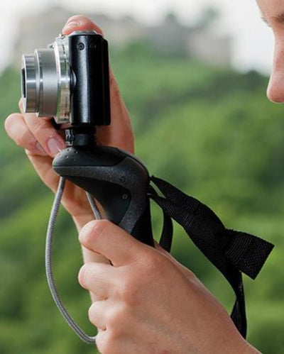 Hand holding a camera with a grip and strap against a blurred green background
