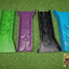 Four decorative plastic shims in green, purple, black, and blue on a green textured surface with a brand logo in the corner.