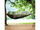 Green hammock with mosquito net hanging between two trees in a forest setting