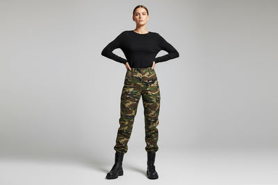 Person wearing black top and camouflage pants on a plain background